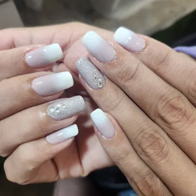 This beautiful ombre manicure blends from a soft nude to a crisp white, with two accent nails fully coated in silver glitter and adorned with rhinestones for extra sparkle.