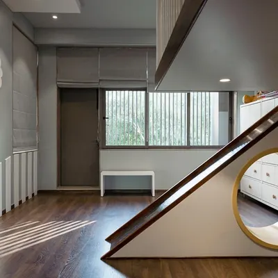 This playful kids' room features a custom-built elevated bed with a slide, designed for endless fun. A circular cutout creates a cozy nook beneath, while the cloud-shaped wall light adds a touch of whimsy. The design balances activity with a calming atmosphere.