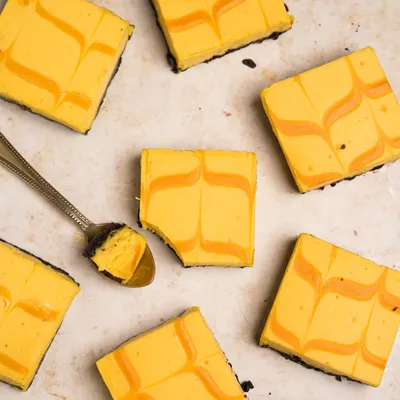 An overhead shot of mango cheesecake bars, creating a beautiful pattern with the swirls. A spoonful is taken out to show the creamy texture.
