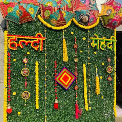 An artificial green wall provides a lush, modern base for this Haldi and Mehndi backdrop. I use real marigold flowers to write out "Haldi" and "Mehndi" and add traditional hangings and colorful Rajasthani umbrellas for a festive look.