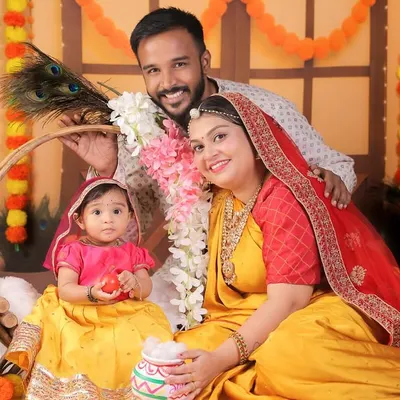 A lovely family portrait from a Radha-themed shoot, with parents and their 8-month-old daughter in coordinated traditional outfits.