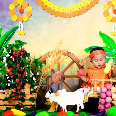 A baby dressed in traditional attire for a Sankranti or harvest festival theme, complete with a bullock cart and fresh produce.