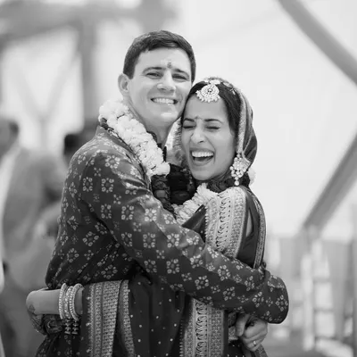 A joyful, candid moment captured in timeless black and white. This image of the American groom and Indian bride sharing a heartfelt laugh and embrace perfectly encapsulates the spirit of their union.