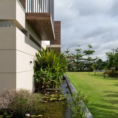 An exterior view of the Celadon residence, showing how the built form is nestled into the lush landscape. The koi pond wraps around the edge of the home, creating a natural moat that connects the structure to the garden.