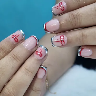 A playful twist on the French manicure, this design features a shiny chrome silver tip and a hand-painted red bow on each nail for a cute and quirky finish.