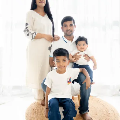 A classic family portrait with parents and two sons. The coordinated white and denim outfits and the bright, clean background create a timeless and fresh look.