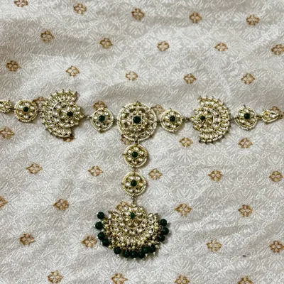 A traditional hair choti accessory for rent, designed with Kundan work and green beads to adorn a long braid.
