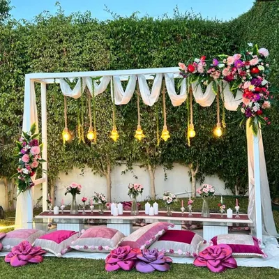 A beautiful sundowner setup for a baby welcome party. I designed this low seating arrangement with plush pink and purple cushions, a floral-adorned canopy with hanging lights, and delicate flower arrangements for a relaxed yet elegant garden party vibe.