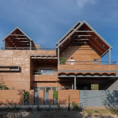 The Madhura residence features a distinctive facade with sloping tile roofs and walls made of CSEB mud blocks. The design merges two family homes on a single urban plot, using arches and vaults to create unique interior volumes.