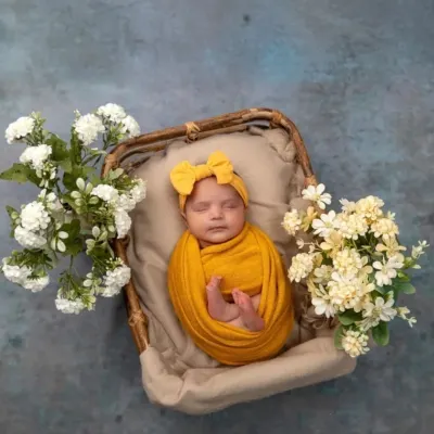 A vision in sunny yellow. This baby girl is nestled in a rustic basket, surrounded by delicate white and yellow flowers, creating a bright and cheerful newborn portrait.