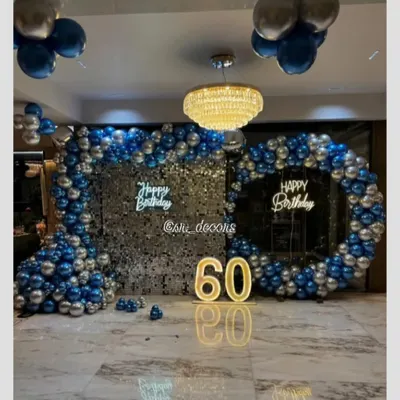 An expansive and luxurious setup for a 60th birthday, featuring two shimmer walls, double neon signs, and a large balloon arch in blue and silver, perfect for a grand celebration.