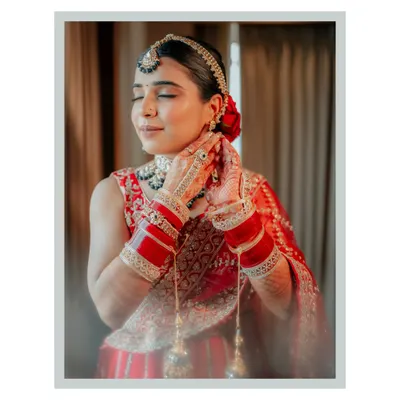 A serene moment as the bride, Neha, closes her eyes, adjusting her earring. The soft lighting and her traditional red attire create a timeless and beautiful portrait.