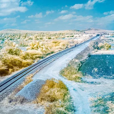 An infrared photograph of a railway line cutting through the landscape. The foliage turns a golden yellow and the sky a vibrant blue, creating a surreal, false-color world.