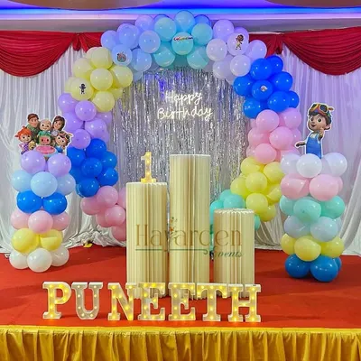 A bright and cheerful Cocomelon theme for a first birthday. This setup features a full balloon arch in pastel colors, character cutouts, and custom marquee letters spelling out the birthday boy's name, Puneeth.