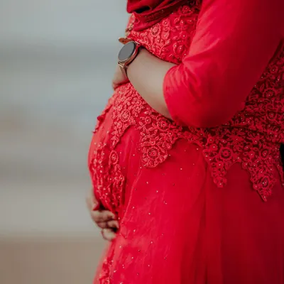 A close-up, artistic shot of a mother-to-be in a vibrant red dress, tenderly holding her baby bump. A beautiful way to capture the journey to motherhood.