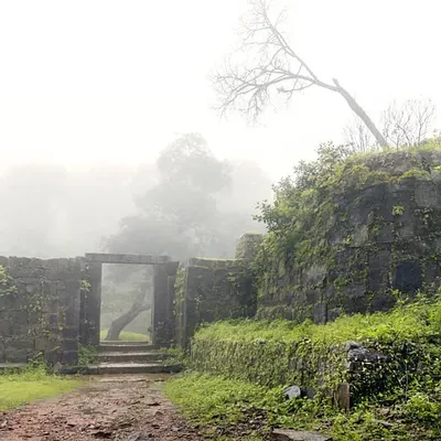The ruins of Kavaledurga Fort on a foggy day. The thick mist covering the landscape gives the ancient stone structures a mysterious and haunting feeling, perfect for a moody fine art photograph.