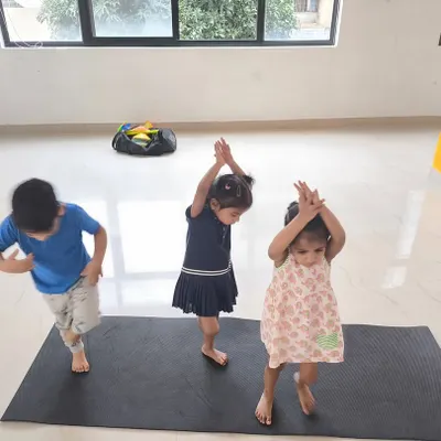 Three young children attempt a gymnastics pose during our indoor fitness class. We use playful imitation to teach basic movements, making learning fun and engaging for toddlers.