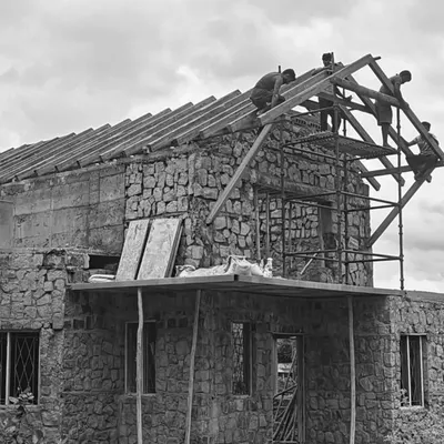 A house takes shape with walls of natural, random rubble stone. Here, workers are installing the wooden framework for a traditional sloping roof, a process that requires precision and teamwork.