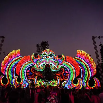 The main stage of a Goa trance music festival at night. The vibrant, psychedelic decor is lit up, showcasing the epic scale and electric atmosphere of the event.