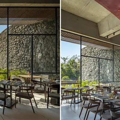 The dining area at the Radisson Resort in Lonavala features floor-to-ceiling windows that look out onto a massive wall of locally sourced stone, blurring the line between interior and exterior.