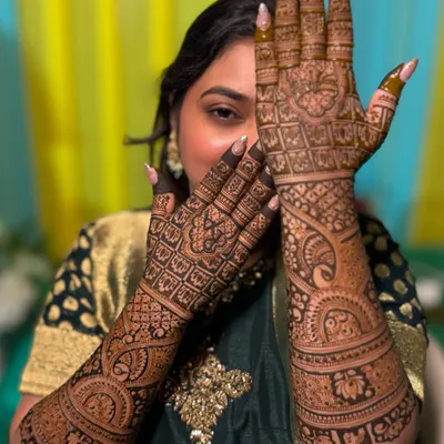 A beautiful bride, Rutuja, showcasing her full bridal mehendi. The design is packed with traditional elements, including intricate jaali (net) patterns, peacocks, and floral bands.