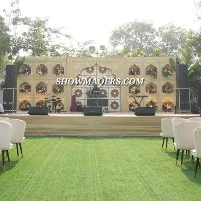 A full view of a stage designed with a "Banaras" theme. The backdrop features intricate archways and niches filled with flowers, creating a culturally rich setting for a daytime corporate event or dealer meet.