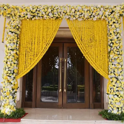 A stunning entrance for a daytime ceremony, featuring pillars covered in white and yellow flowers and curtains made of traditional marigold garlands.