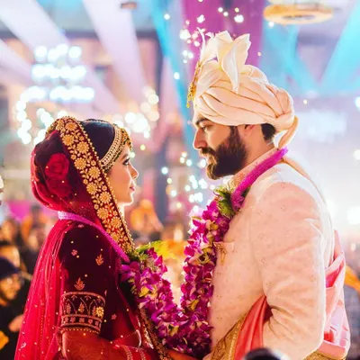 The quintessential Varmala moment. We capture the intense, loving gaze between the couple as they exchange garlands, surrounded by the grand decor and warm lights of their ceremony.