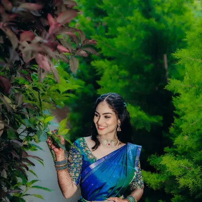 A beautiful outdoor shot of the bride-to-be. The natural greenery provides a stunning backdrop for her vibrant blue and green saree and the soft, glowing makeup I created for her engagement.