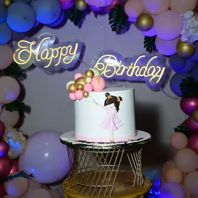 A chic and modern birthday cake setup. The simple, elegant cake is perfectly complemented by a gold wire stand and a stylish neon "Happy Birthday" sign.