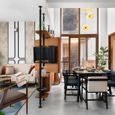 The open-plan living and dining area of the Raghavan Valley home. The space is visually divided by a custom wood and metal shelving unit that also houses a rotating television, allowing for flexible viewing from either the living or dining space.