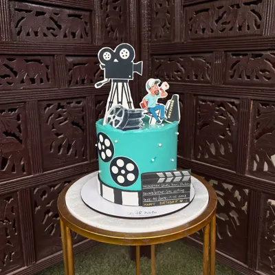 Lights, camera, action! This movie director-themed cake is perfect for a film enthusiast, complete with a camera, film reels, and a personalized clapperboard, all made from edible materials.