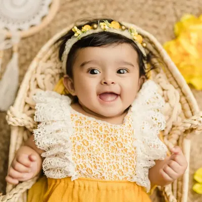 A happy 6-month-old baby girl with a bright, infectious smile. This close-up from her sitter session captures her personality perfectly in a cheerful yellow-themed setup.