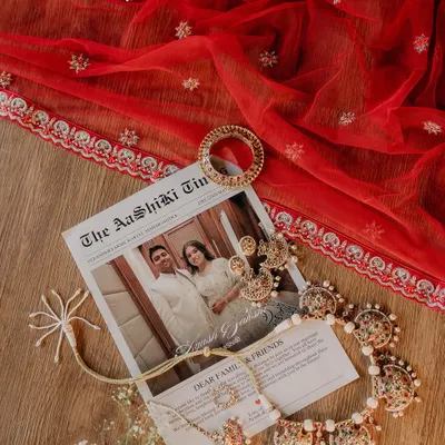 A flat lay of the bride's accessories, including her jewelry and a custom newspaper invitation, set against her red wedding veil.