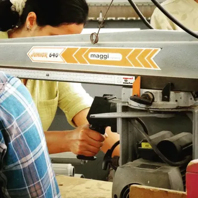 A close-up of a student operating a radial arm saw, highlighting the focus and precision required for machine woodworking.