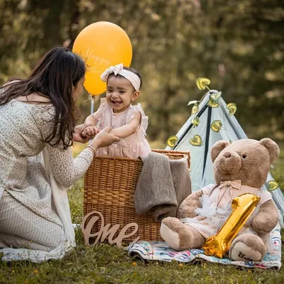 A beautiful, candid moment as a mother shares a laugh with her daughter on her first birthday. The outdoor setting in the mountains provides a stunning, natural backdrop for these family interactions.
