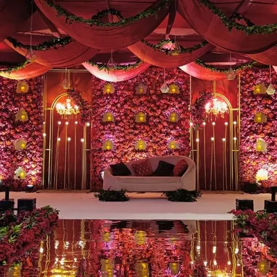 A stage that is a symbol of timeless elegance. We created this opulent backdrop with layers of plush red fabrics, a wall of cascading florals, and warm golden accents for a truly grand reception.