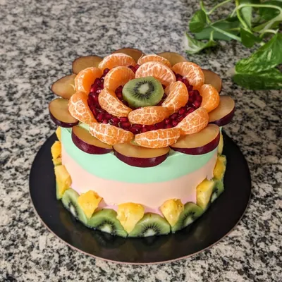 Fruits are nature's candies! This fruit-overloaded cake features a beautiful floral arrangement of plums, oranges, pomegranates, and kiwi on a tri-color cream frosting.