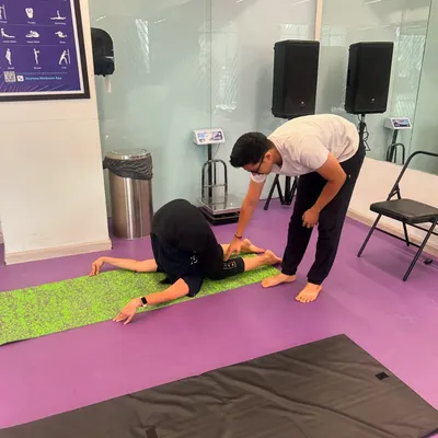 A student practices Halasana (Plow Pose) in my gym class. I'm providing a gentle adjustment to help her deepen the pose and release tension in her neck and shoulders.