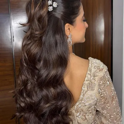 A glamorous half-up ponytail with voluminous, cascading waves and delicate floral clips. This style is perfect for a cocktail party or reception, offering a look that is both chic and modern.