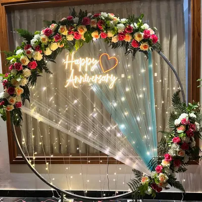A full view of the elegant floral anniversary ring backdrop. The combination of fresh flowers, a neon sign, and fairy lights creates a beautiful focal point for any anniversary party.