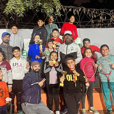 The future of tennis is bright. Here is a large group of our junior players and coaches celebrating their wins at an open tournament, with everyone beaming with pride, holding their trophies and medals.