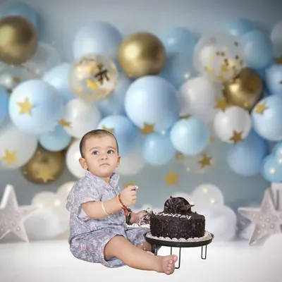A classic cake smash setup for a first birthday. The baby is ready to dig into the cake against a backdrop of blue and gold balloons.