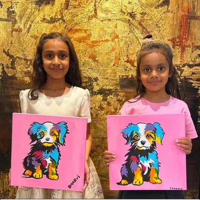 Joyful beginnings start here, where little hands learn big expressions. These two young artists are proudly holding up their colorful pop-art style dog paintings.