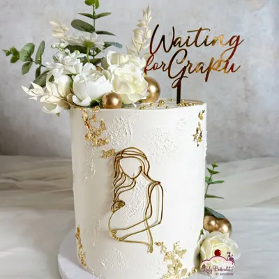 A sophisticated and elegant baby shower cake. The design is clean and modern, with textured white buttercream, gold leaf, and a beautiful "Waiting for Grapin" topper.