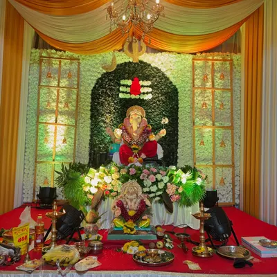 A beautiful Ganpati decoration with a backdrop of white flowers forming a Shivling. I used yellow and white drapes, a hanging chandelier, and spotlights to create a divine setting for the idol.