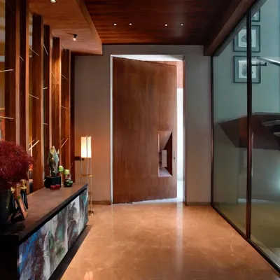 The entrance to a contemporary Gurgaon home, featuring a massive, custom-designed wooden pivot door. The adjoining console and art piece set a tone of sophisticated, artistic living from the moment you step inside.