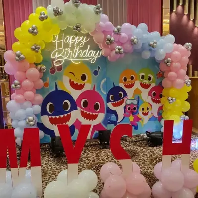 A colorful Baby Shark themed birthday party, featuring a character backdrop, a pastel balloon arch, and large custom letters.