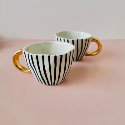 A close-up of the premium ceramic cups with elegant black stripes and a luxurious golden handle, a popular item in our hampers.