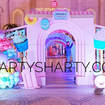 A spectacular entrance to a 'Candyland' party, with giant cupcake and ice cream props, and a tunnel of rainbow balloon arches.